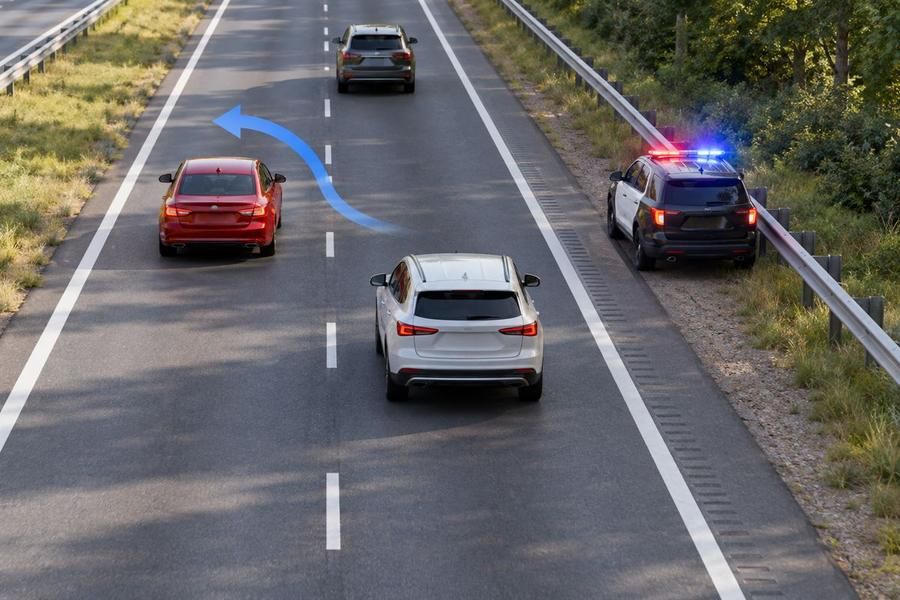 A police car with red and blue lights is stopped on the right shoulder of a highway with two lanes in this direction; a white car drives in the right lane and a red car in the left lane, with a blue arrow showing a move to the left.